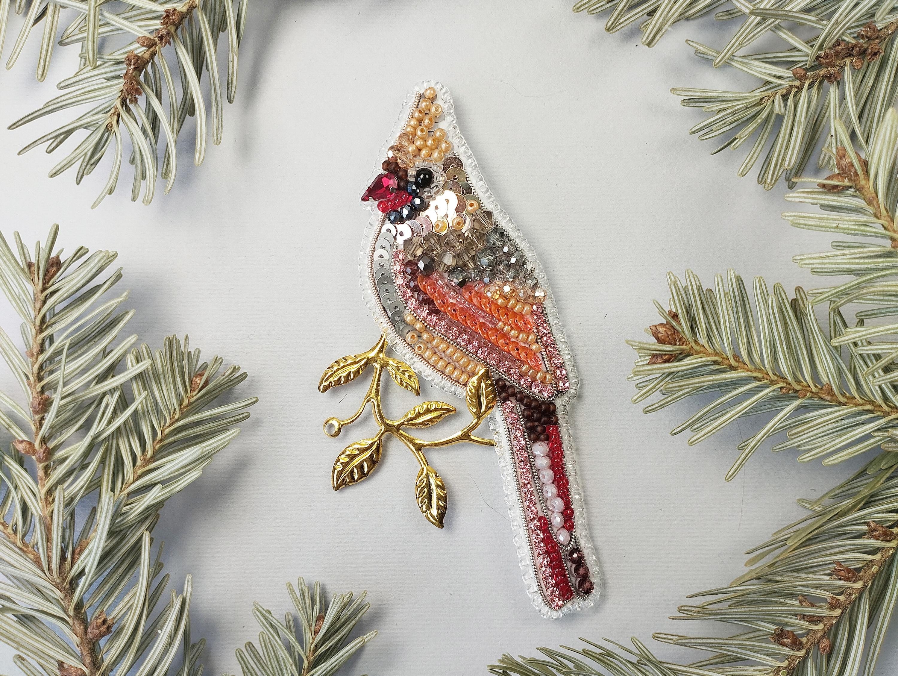 a beaded bird ornament hanging from a pine branch